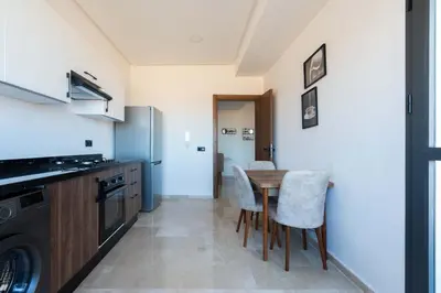 a kitchen with a table and chairs and a refrigerator at Appartement Sublime avec Piscine in Mansouria