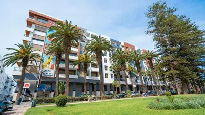 a large building with palm trees in front of it at Charmant appartement joyau du parc 200m plage in Mohammedia