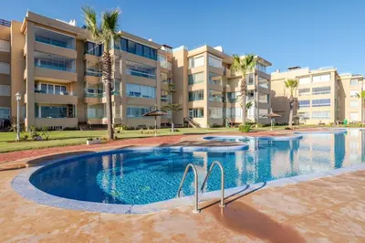 a swimming pool in front of a building with palm trees at Appartement de Luxe - Piscine et Accès à la Plage in Bouznika