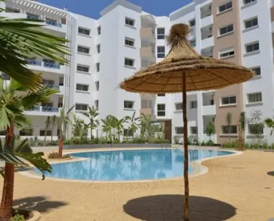 an umbrella and a swimming pool in front of a building at Appartement de luxe à 3 min de l aéroport in Nouaseur