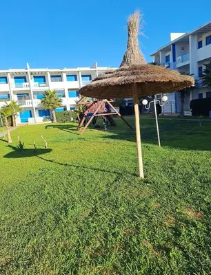 a straw umbrella in the grass in front of a building at appartement à Mansouria avec piscine et accès a la mer Perla Andaloussia El Mansouria in Mansouria