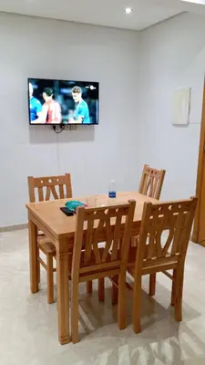 a wooden table and chairs with a television on a wall at Bel Appartement Confort et Commodités au Cœur de Casablanca Belvédère in Casablanca