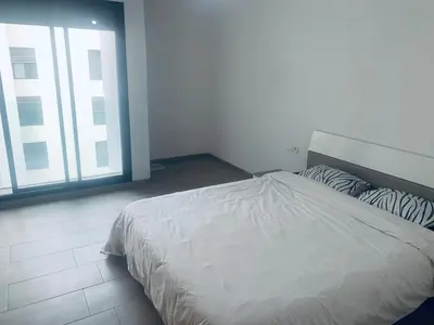 a white bed in a room with a large window at Appartement avec une Chambre, Salon, Salle de Bain et Piscine in El Harhoura