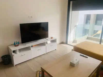 a living room with a flat screen tv on a white cabinet at Appartement avec une Chambre, Salon, Salle de Bain et Piscine in El Harhoura