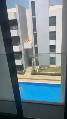 a view of a swimming pool through a window at Appartement avec une Chambre, Salon, Salle de Bain et Piscine in El Harhoura