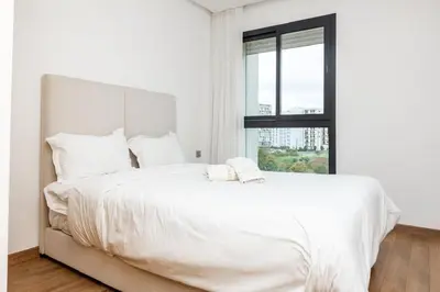 a white bedroom with a large white bed with a window at Luxurious and comfortable in Prestigia in Rabat