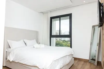a white bedroom with a white bed and a window at Luxurious and comfortable in Prestigia in Rabat