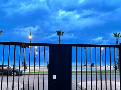 a black fence with palm trees and a beach at Beachfront apartment in Rabat