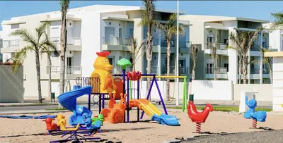 a playground in the sand in front of a building at CASABAY Sidi Rahal, appartement avec accès direct à la piscine in Sidi Rahal