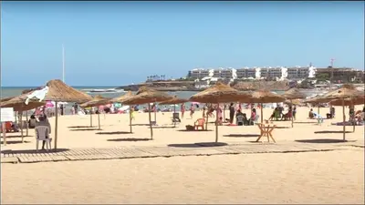 a beach with many straw umbrellas and people on it at Apartment with pool view, 1 min to beach, private parking in Mansouria