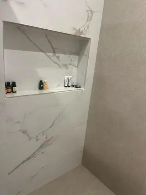 a bathroom with white marble walls and a shelf at Furnished studio with pool in Nouaseur