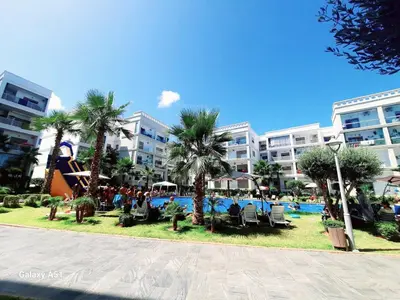 a resort with a pool and some palm trees and buildings at Appartement vue piscine à 3min de la plage bouznika in Bouznika