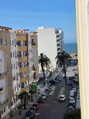 a city street with parked cars and palm trees at Spacieux appartement proche de la mer in Casablanca