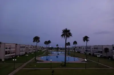 a pool in a park with palm trees and buildings at Ola blanca 1 enjoy in Sidi Rahal