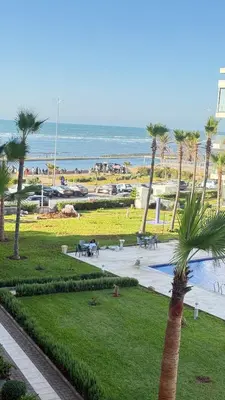 a park with palm trees and a pool and the ocean at luxury apartement en el mansouria in Pont Blondin