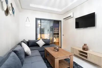 a living room with a couch and a tv at Appartement 2 Chambres à Coté avec Grand Balcon, Piscine, Aire de Jeux pour Enfants et Jardin in Casablanca
