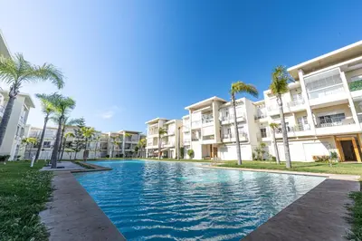 a swimming pool in front of a building with palm trees at Welcome Sidi Rehal Escape King Bed Res Casabay in Sidi Rahal