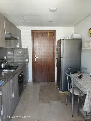 a kitchen with a stainless steel refrigerator and a table at Appart Haut Standing, Très Calm à Nouaceur, Parking, Piscine, à 4min de l'Aéroport in Casablanca