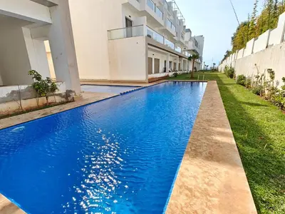 a blue swimming pool in front of a building at Appart Moderne Vue mer latérale & piscine - Plage des Sablettes El Mansouria in O Ben Slimane
