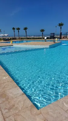 a blue swimming pool with palm trees in the background at Sidi Rahal Blue View 3, front mer, accès plage 1 Piscine in Sidi Rahal