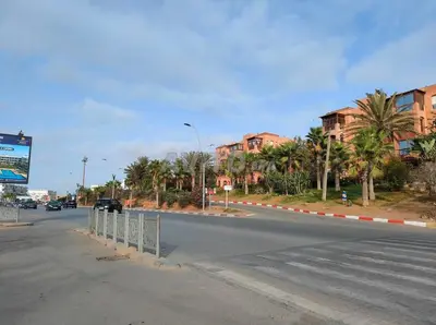 a street with a road with palm trees and buildings at Joli appartement Ricoflores El Mansouria in O Ben Slimane