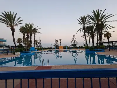 a swimming pool with palm trees and a fence at Chez Bouchra in Mansouria