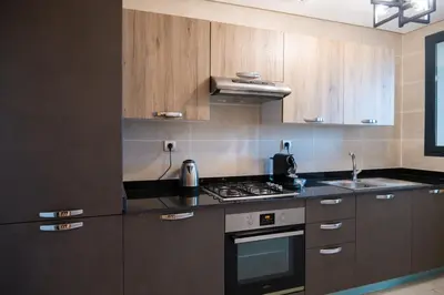 a kitchen with wooden cabinets and a stove top oven at 2BR Prestigia Hay Riad 13 mintues city center in Rabat