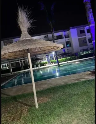 a straw umbrella sitting next to a pool at night at Marbella Beach apartement holiday 2 chambres,piscine et plage in Mansouria