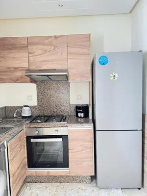 a kitchen with a white refrigerator and wooden cabinets at Bright Apt with Balcony, WiFi, Parking and Pool Resort in Bouznika