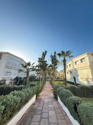 a walkway in a park with palm trees and buildings at Les Perles de Tamaris Beach access Pools in Casablanca