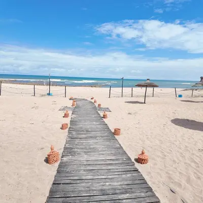 a wooden pathway on the beach with an umbrella at Appartement Tamaris avec piscine et plage privée in Casablanca