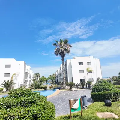 a palm tree in front of two white buildings at Appartement Tamaris avec piscine et plage privée in Casablanca