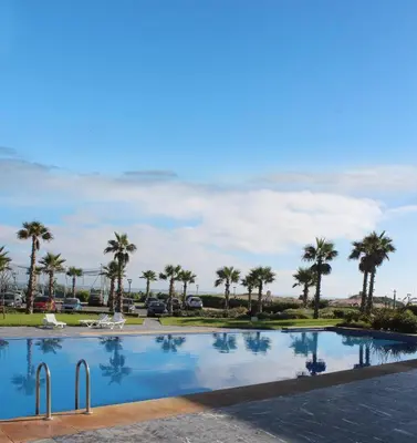 a large swimming pool with palm trees in the background at GARDEN BAY Appartement Luxe Front de Mer à Tamaris Sidi Rahal, Plage Privée, Piscine et Loisirs in Tamaris
