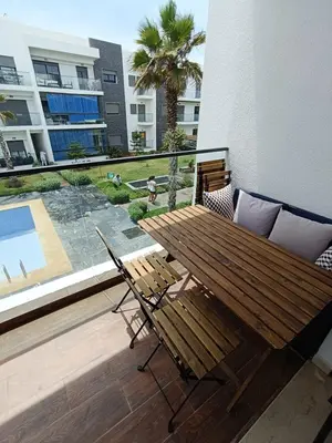 a patio with a wooden table and chairs on a balcony at GARDEN BAY Appartement Luxe Front de Mer à Tamaris Sidi Rahal, Plage Privée, Piscine et Loisirs in Tamaris