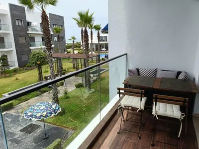 a balcony with a table and chairs and palm trees at GARDEN BAY Appartement Luxe Front de Mer à Tamaris Sidi Rahal, Plage Privée, Piscine et Loisirs in Tamaris