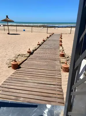 a wooden walkway on a beach next to the ocean at GARDEN BAY Appartement Luxe Front de Mer à Tamaris Sidi Rahal, Plage Privée, Piscine et Loisirs in Tamaris