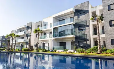 an apartment building with a swimming pool and palm trees at GARDEN BAY Appartement Luxe Front de Mer à Tamaris Sidi Rahal, Plage Privée, Piscine et Loisirs in Tamaris