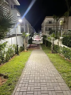 a walkway with palm trees and buildings at night at Beautiful apartment with pool in Mansouria