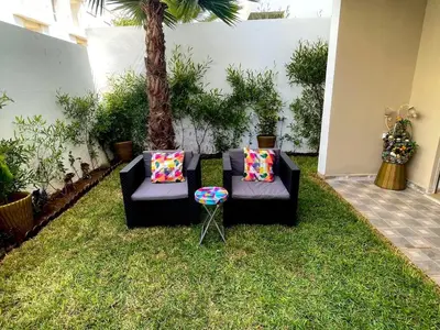 a garden with two couches and a palm tree at Seaside escape beautiful garden apartment in Sidi Rahal