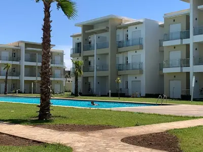 a large apartment building with a swimming pool and a palm tree at Casabay Sidi Rahal, à 2mn de la mer en bord de piscine et jardin in Sidi Rahal