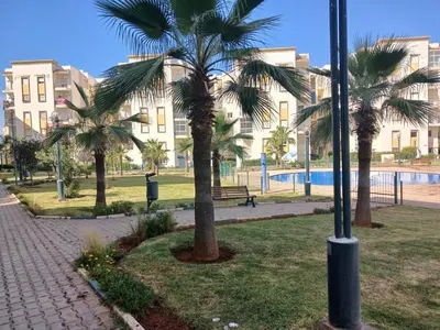 a park with palm trees in front of a building at appartement 75m2 avec piscine in Bouznika