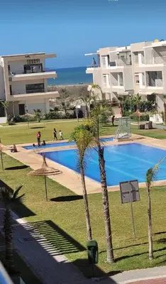 a swimming pool with palm trees in front of a building at Maison vacances Mansoria in Casablanca