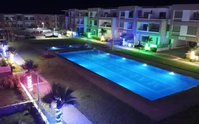 a swimming pool at night with palm trees and buildings at Maison vacances Mansoria in Casablanca