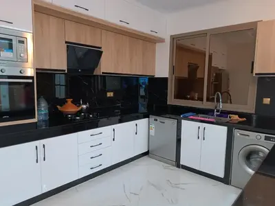 a kitchen with white cabinets and black counter tops at Jolie appartement Bouznika in Bouznika