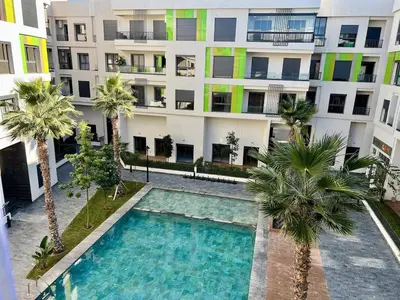 an apartment building with a swimming pool and palm trees at Natura Living Apartment in Mohammedia
