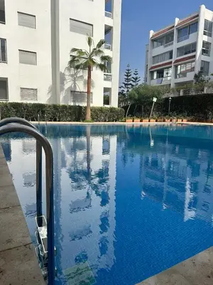 a swimming pool with a palm tree and a building at Studio bord de mer , La Siesta Beach Resort in Mohammedia