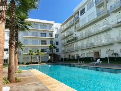 a swimming pool in front of a large apartment building at Appartement Kettani bouznika in Bouznika