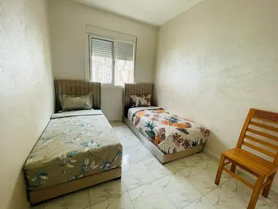 a bedroom with two beds and a chair and a window at Appartement cosy avec vue jardin à Casablanca ! in Casablanca