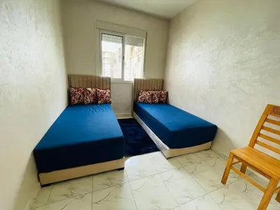 two beds in a room with a chair and a window at Appartement cosy avec vue jardin à Casablanca ! in Casablanca