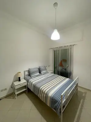 a white bedroom with a bed and a night stand at Al kawtar Vacation apartment in Mansouria in O Ben Slimane